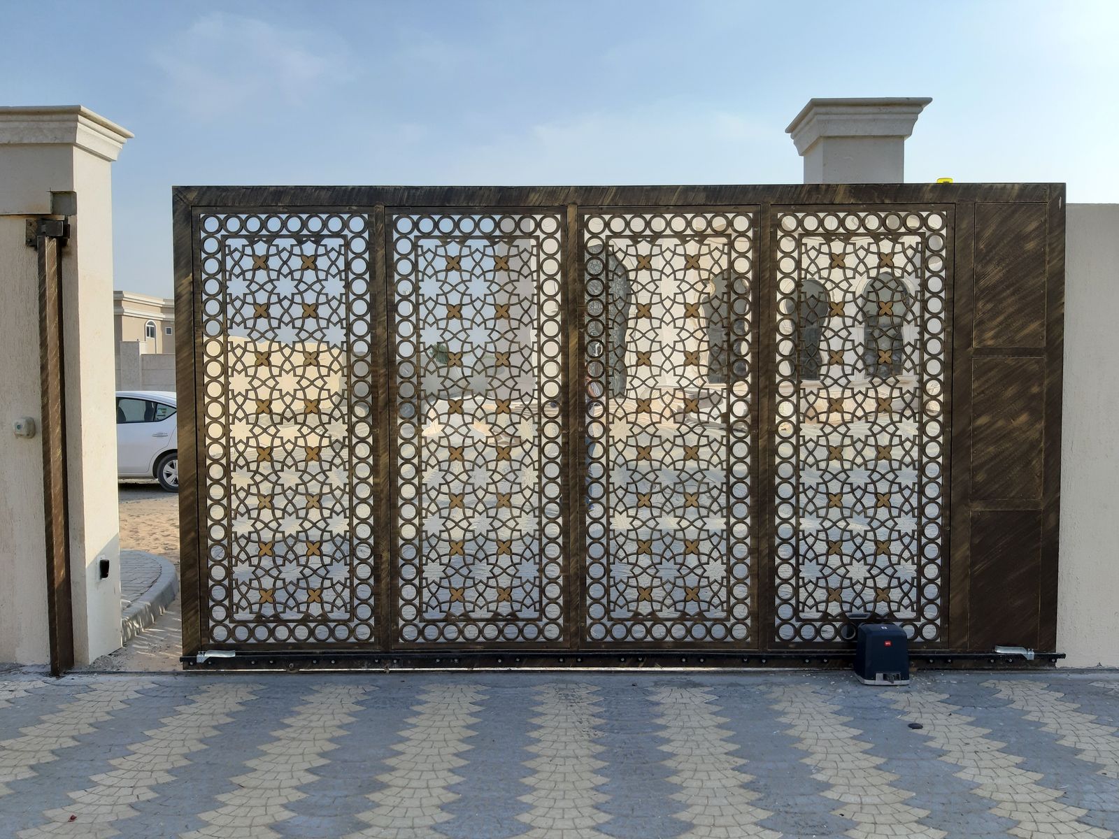 Automatic slide gate operator mounted at the base of a large decorative metal gate on a gear rack