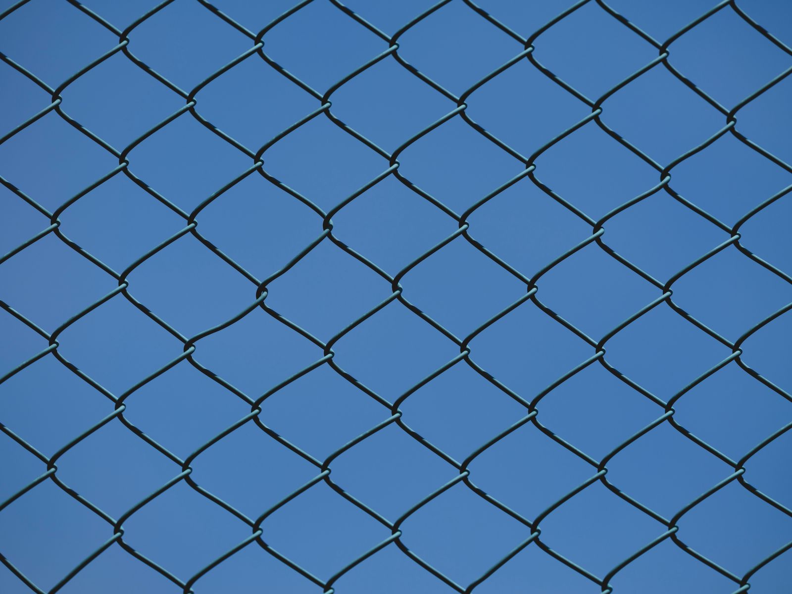 Close-up of chain link diamond mesh against a clear blue sky