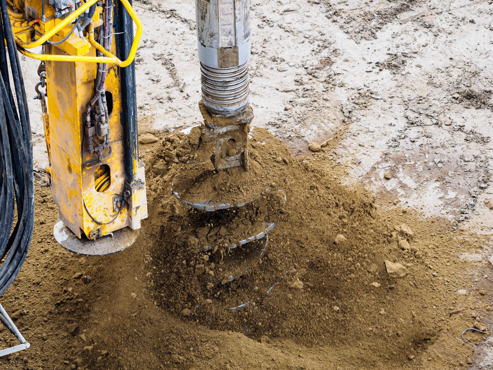 Hydraulic auger with a rock bit boring a fence post hole through hard, rocky soil