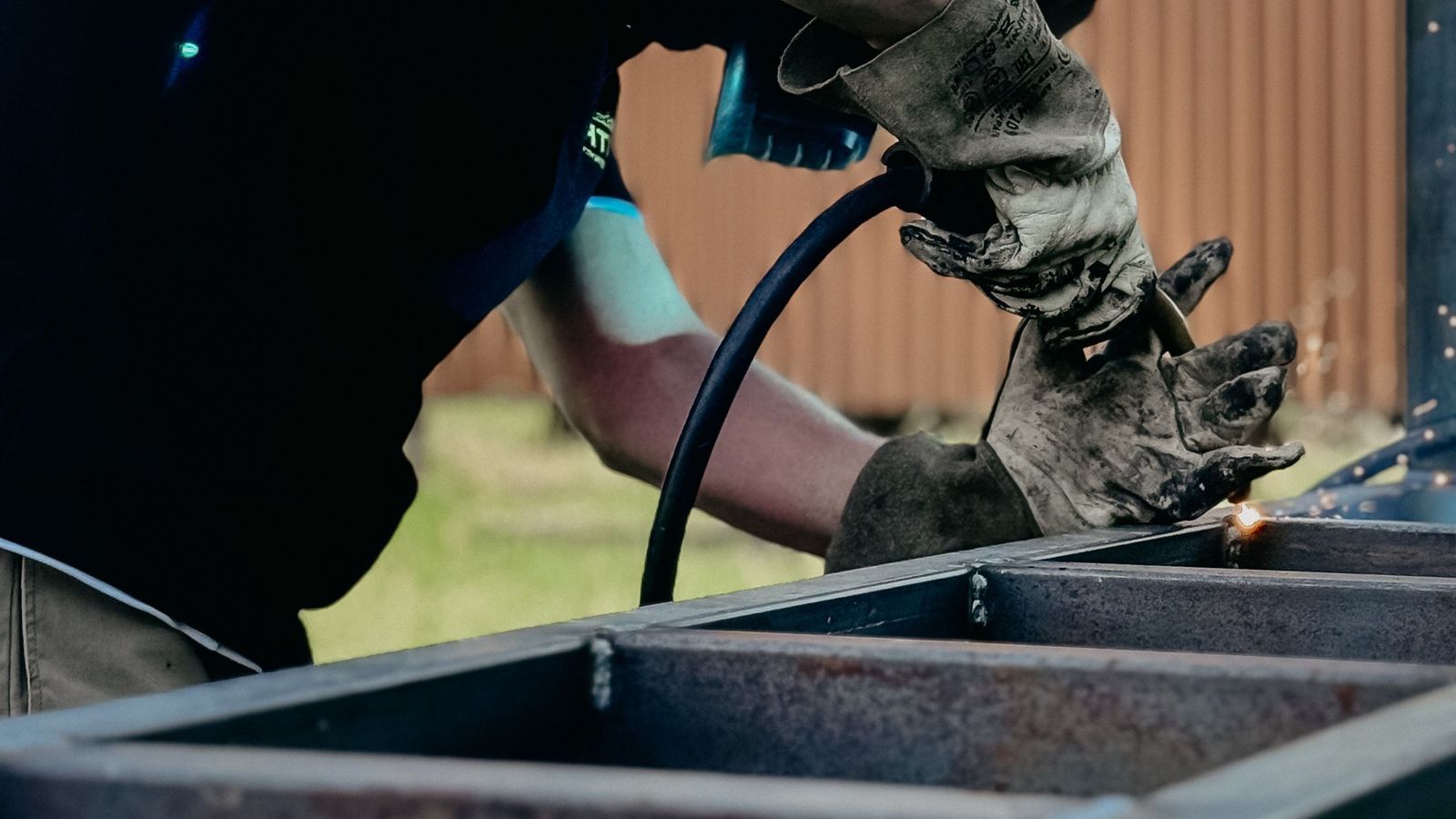 Welder in gloves and helmet welding the corner of a steel gate frame outdoors