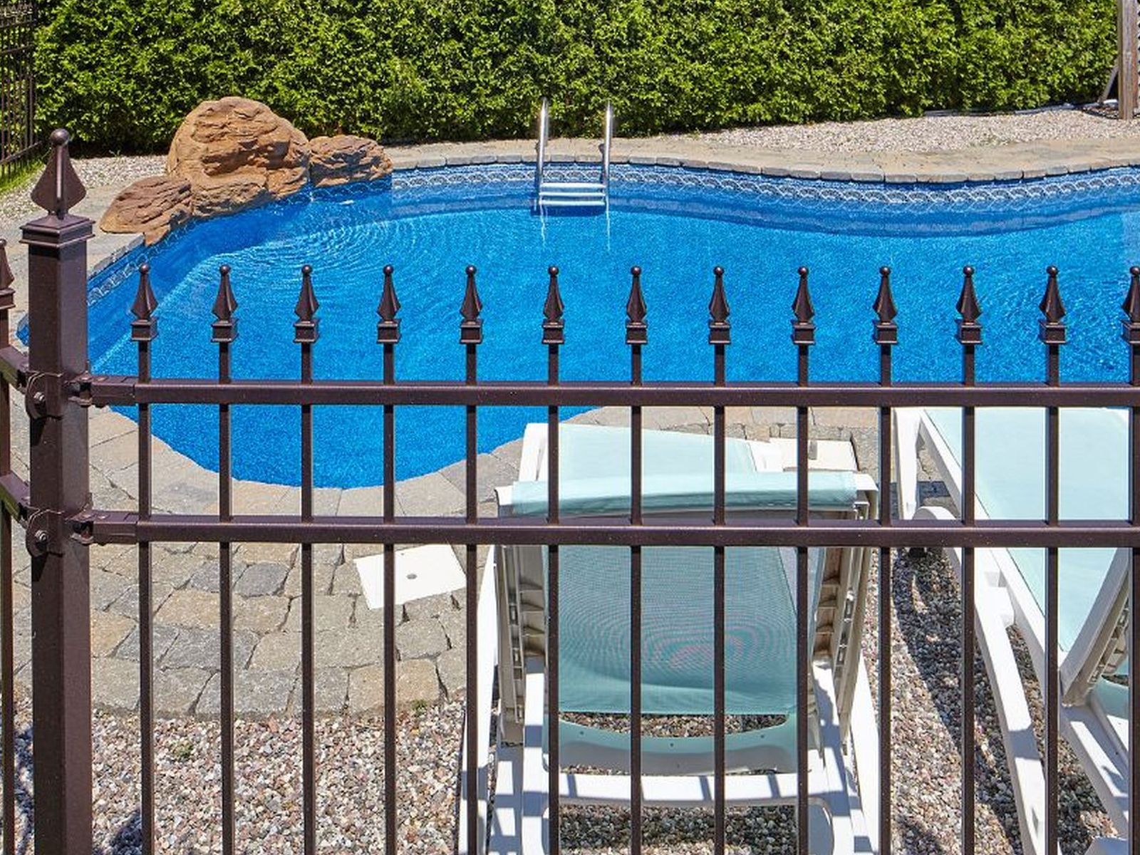 Bronze powder-coated metal pool fence with spear-top pickets around an in-ground pool with rock landscaping