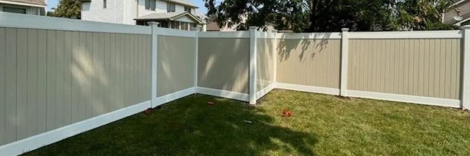Tan vinyl privacy fence with white posts and post caps turning a corner around a backyard