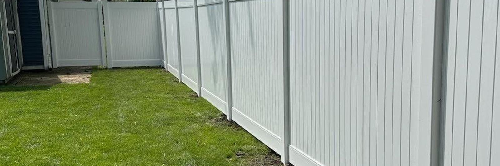 White vinyl privacy fence running along a grassy backyard