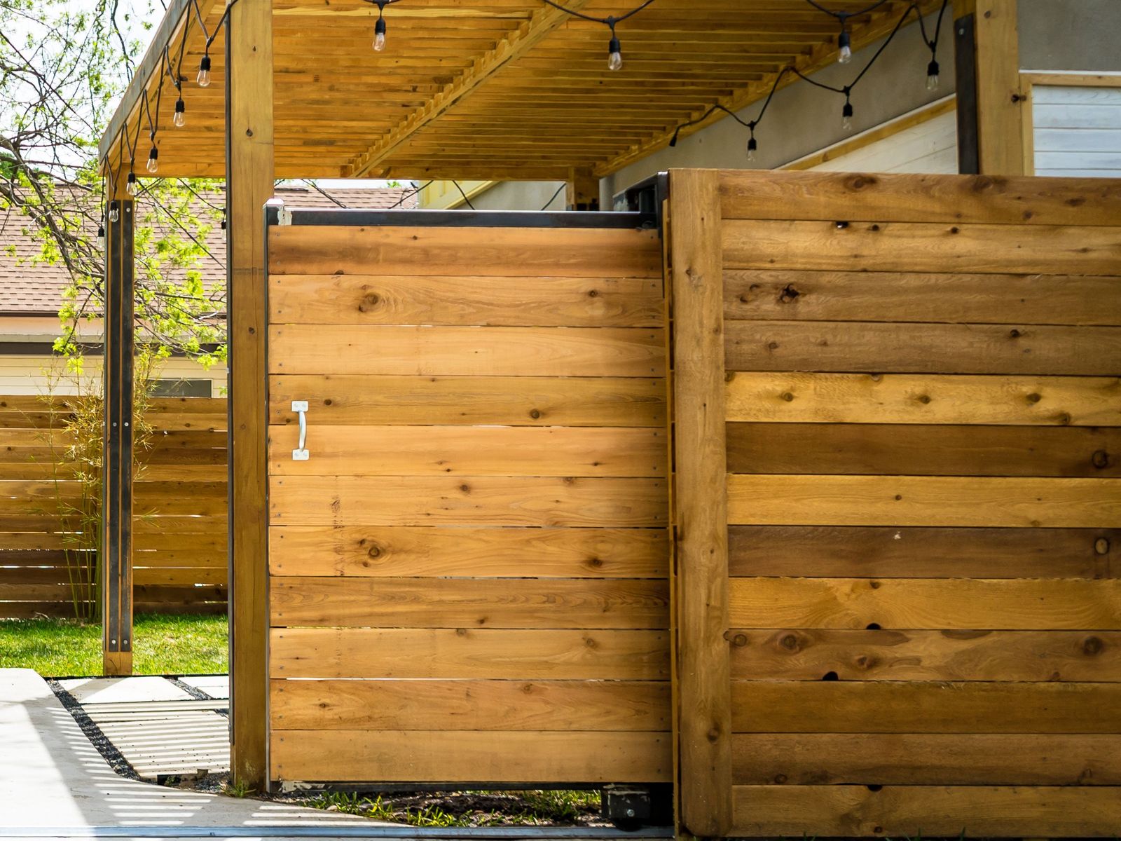 Horizontal cedar slide gate on a steel frame, rolling across a concrete drive between wood fence panels
